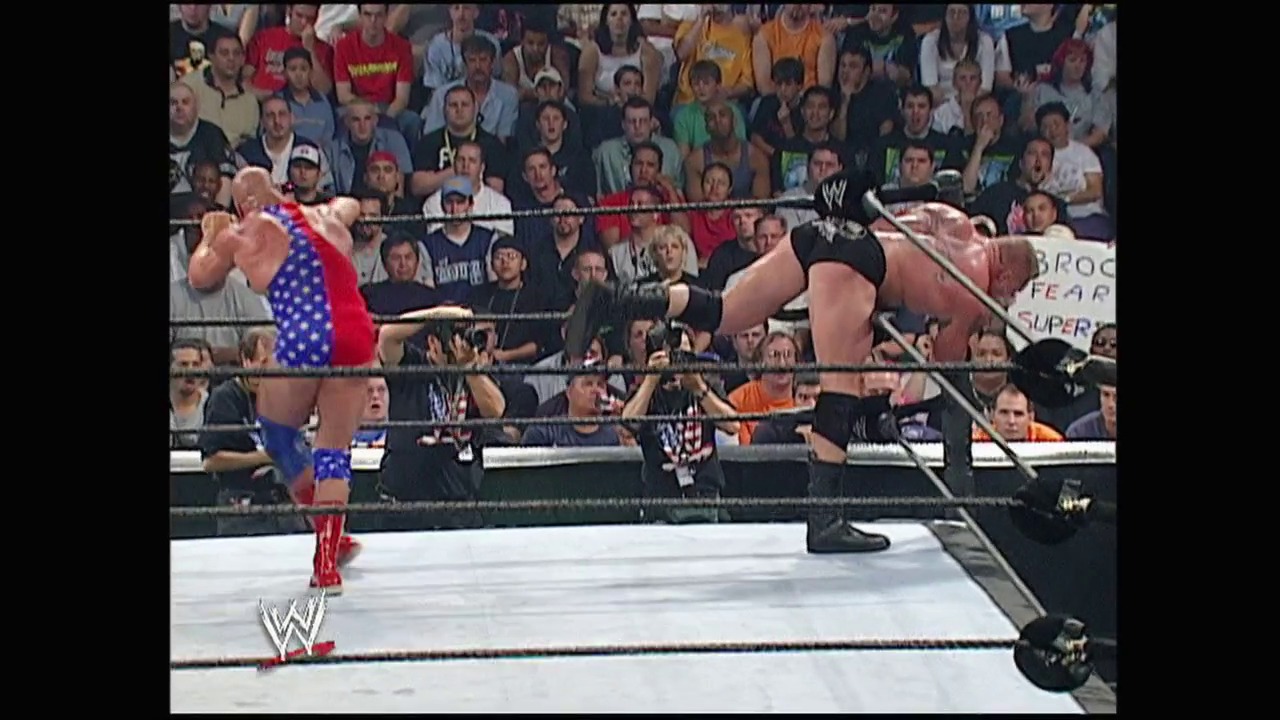 A frame from Summerslam (2003) at 1:33:53. Two WWE wrestlers engage in combat within the ring during SummerSlam 2003, with one competitor in patriotic red and blue attire facing off against another in black. The packed arena crowd watches intently from the stands, with the WWE logo visible on the ring apron.