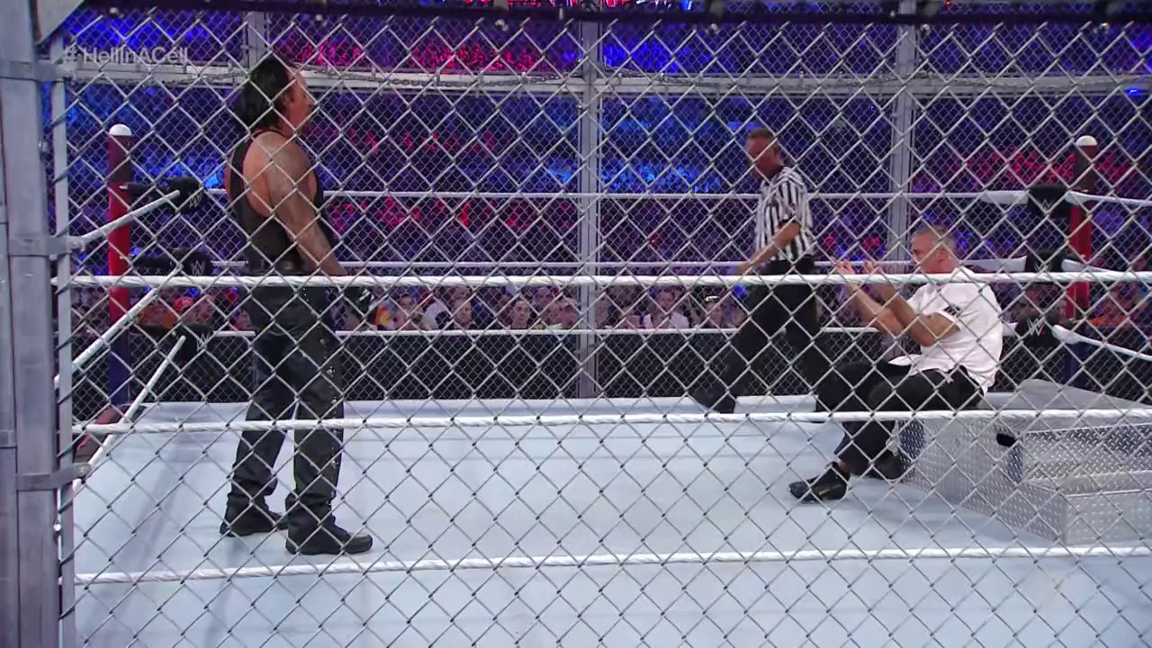A frame from WrestleMania 32 (2016) at 2:45:29. # WrestleMania 32 Hell in a Cell Match

Inside a steel cage, wrestlers grapple in the ring while a referee oversees the action. The crowd fills the arena in the background, illuminated by blue and pink lighting, with "WrestleMania" branding visible at the top.