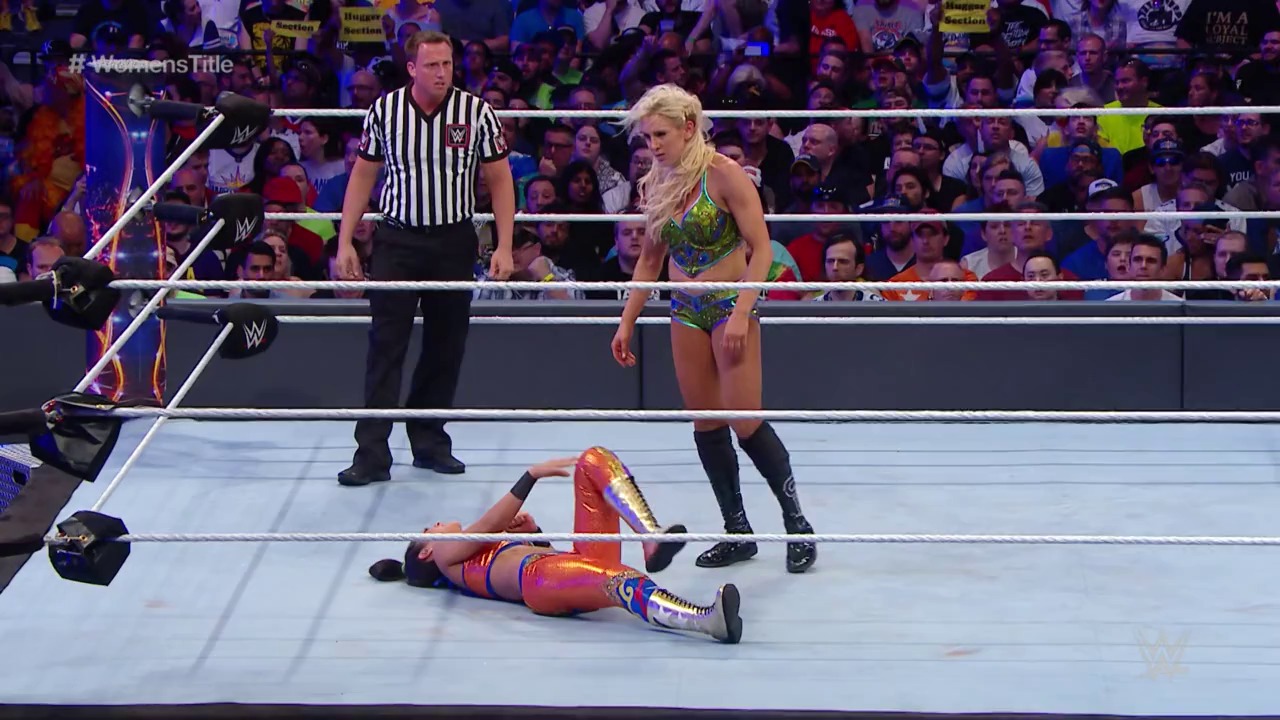 A frame from WrestleMania 33 (2017) at 1:26:53. # WrestleMania 33 Match Scene

A female wrestler in green and gold attire stands over her opponent lying on the mat in red and blue gear, while a referee in striped shirt observes. The crowd fills the arena behind the white-roped ring, with "#WomensTitle" visible on the broadcast graphics.