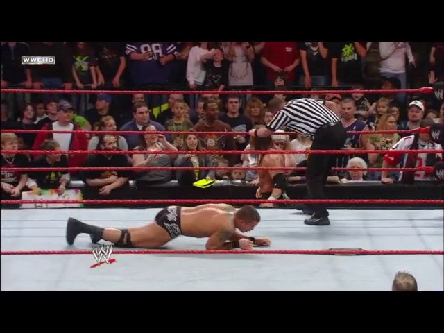 A frame from WWE Raw (March 3, 2008) at 1:27:09. A wrestler performs a push-up position move in the WWE ring while a referee in striped shirt stands nearby. The crowd fills the arena stands in the background, with the WWE logo visible on the mat.