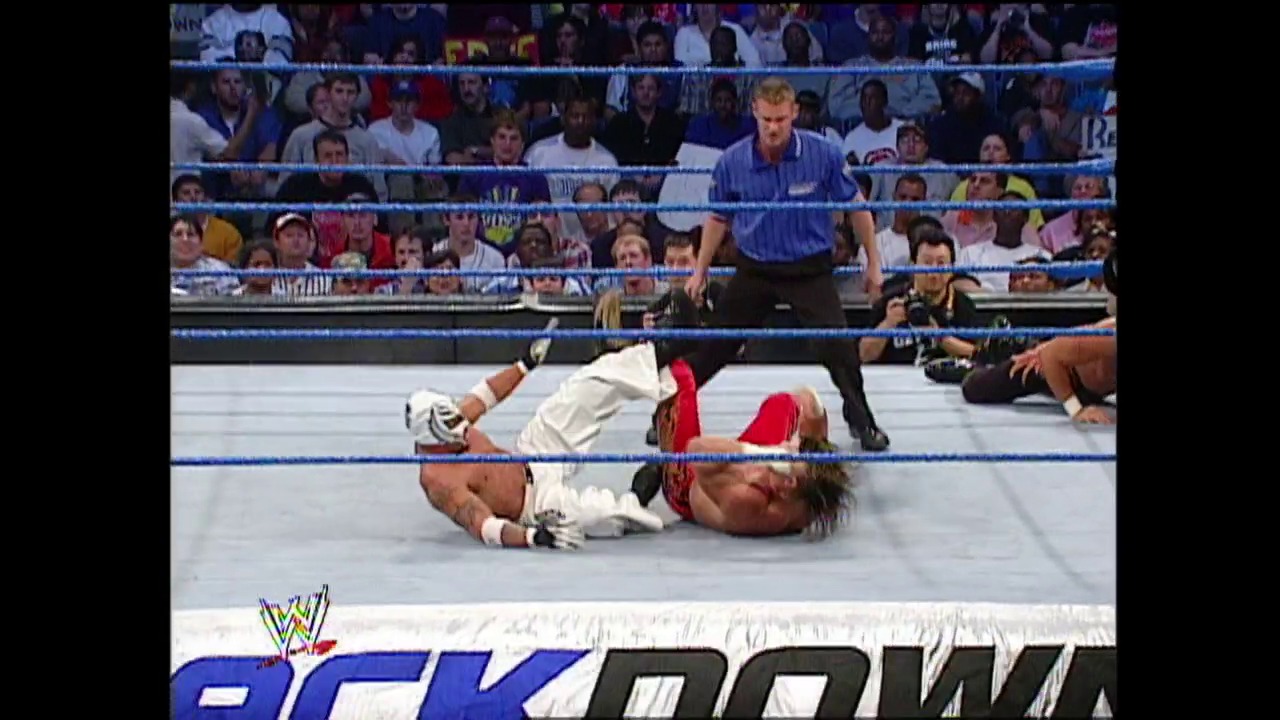 A frame from WWE Raw (October 24, 2002) at 36:07. A WWE wrestler lies on the mat wearing red and white attire while a referee stands nearby. The crowd fills the arena stands behind the blue ropes, with the SmackDown logo visible at the bottom of the screen.