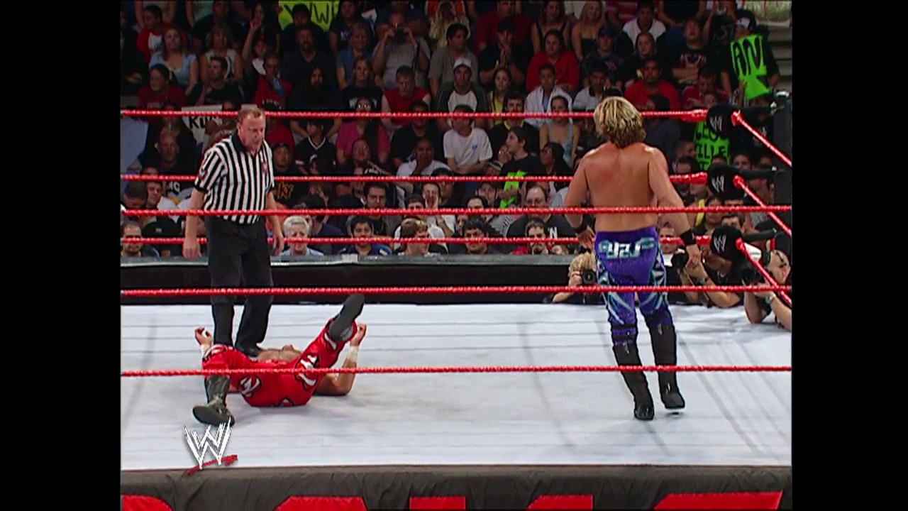 A frame from WWE Raw (September 20, 2004) at 39:58. A WWE Raw match in progress inside a red-roped ring, with one wrestler down on the mat in red attire while another stands nearby. A referee in black and white stripes officiates as the crowd watches from the stands behind the ropes.