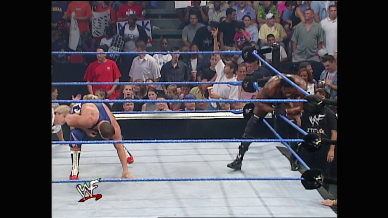 A frame from WWE SmackDown (August 30, 2001) at 1:15:55. A WWE wrestler in blue and red attire bends over in the ring while an opponent in black stands nearby, with the crowd visible behind the blue ropes and the WWF logo displayed in the corner.
