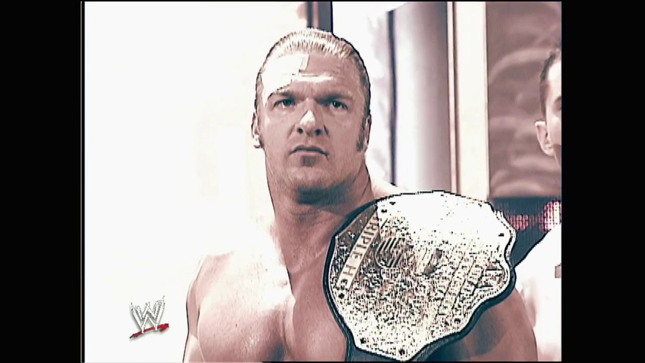 A frame from WWE Unforgiven (2003) at 2:21:36. A professional wrestler displays a championship belt while wearing a bandage on his forehead. The WWE logo appears in the lower left corner of the frame.