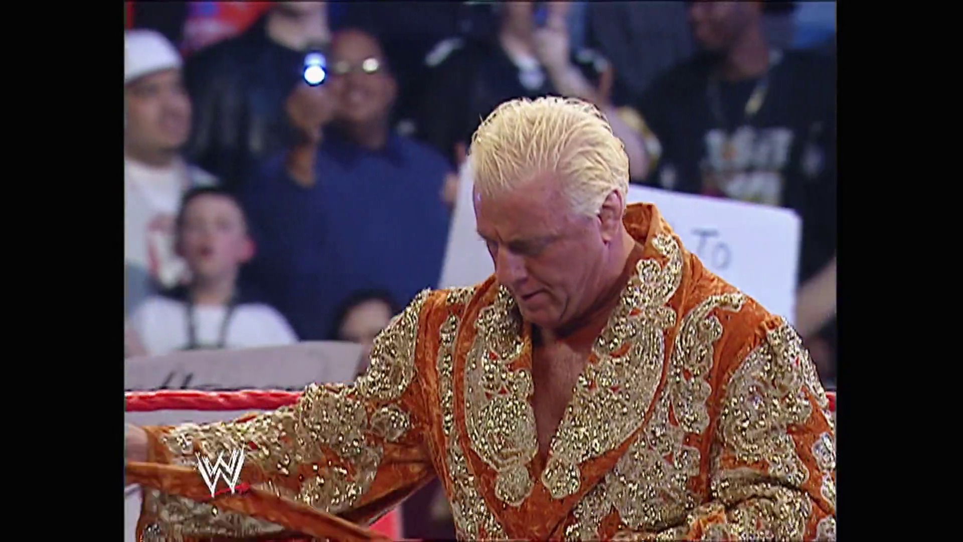 A frame from WWE Raw (February 6, 2006) at 37:18. A wrestler in an ornate orange and gold embroidered robe stands in the WWE ring with the crowd visible in the background. The WWE logo appears in the bottom left corner of the broadcast.