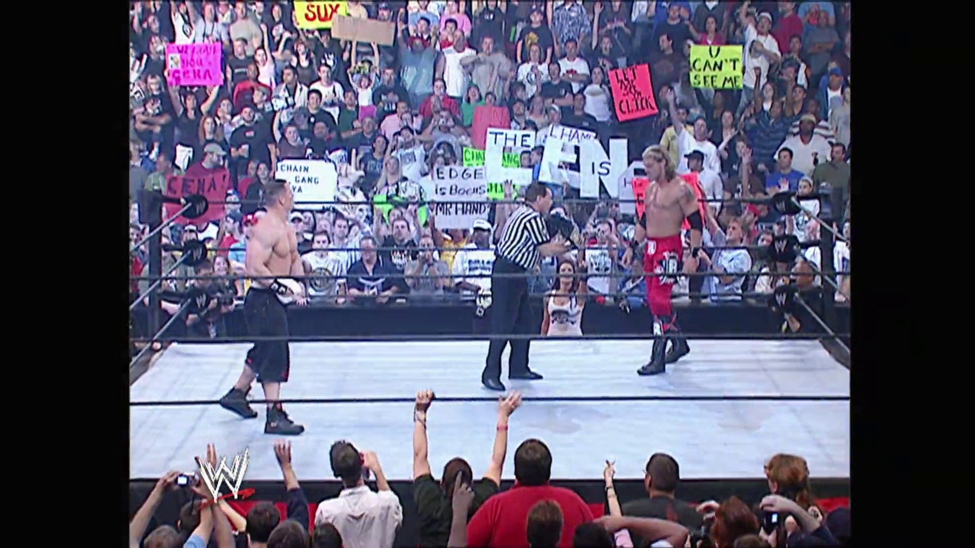 A frame from WWE Raw (January 30, 2006) at 1:16:05. # WWE Raw Wrestling Match

A professional wrestling match is underway in a packed arena, with two shirtless wrestlers in the ring and a referee in striped shirt. The energetic crowd holds colorful signs and phones, with WWE graphics and branding visible throughout the venue.