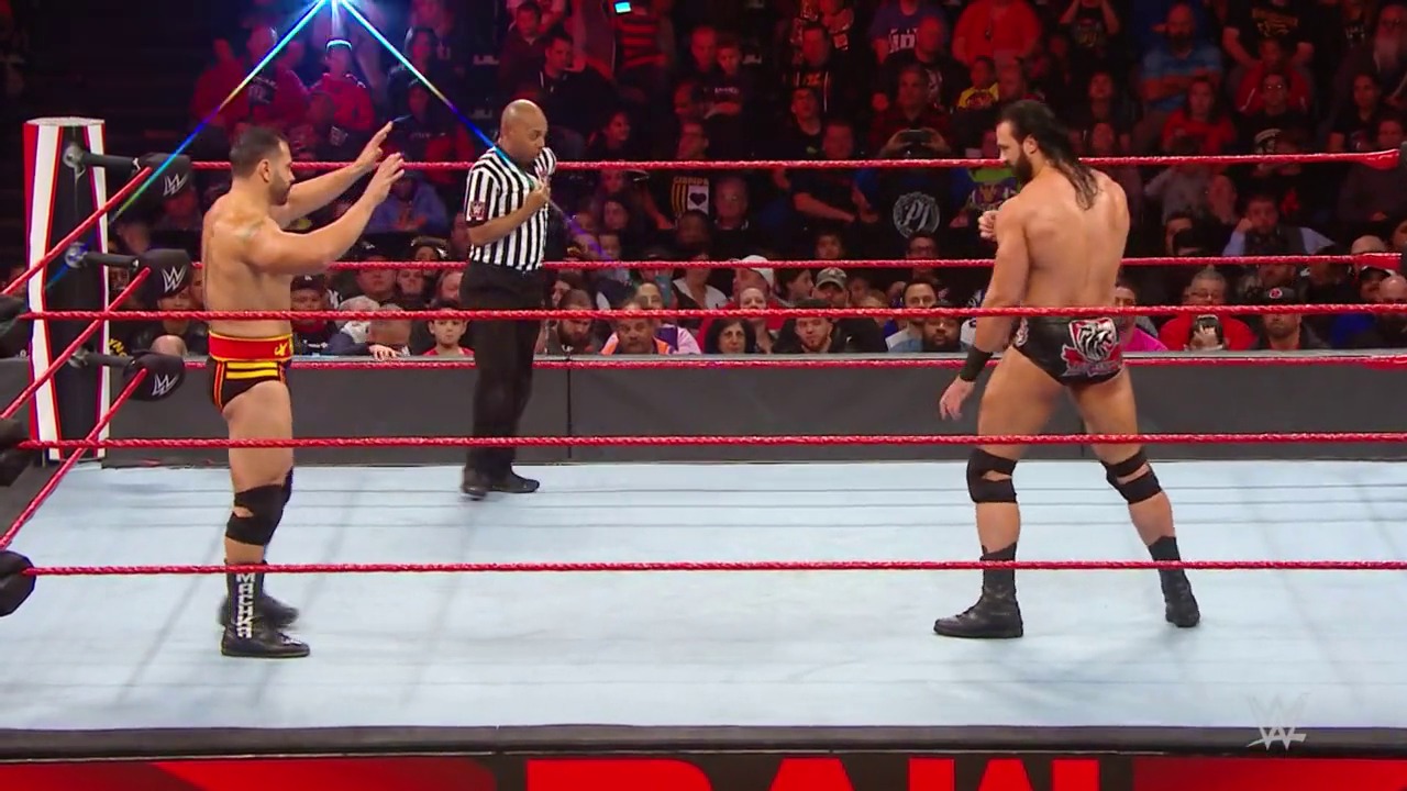 A frame from WWE Raw (November 4, 2019) at 1:12:35. Two wrestlers face off in a WWE Raw match inside the iconic red-roped ring, with a referee in striped shirt between them. The arena is filled with enthusiastic fans in the background, creating an electric atmosphere for the televised event.