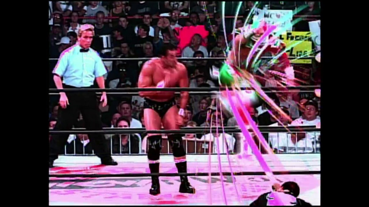 A frame from WWE SmackDown (June 5, 2003) at 46:01. A wrestling match is in progress inside a WWE ring, with a shirtless wrestler standing while an opponent lies on the mat. A referee in a light blue shirt observes the action, and vibrant pink and green graphics overlay the scene as the crowd watches from the stands.