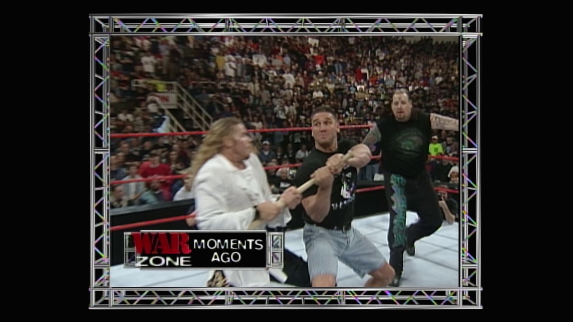 A frame from WWE Raw (April 12, 1999) at 53:48. # WWE Raw - War Zone Moment

A wrestler in a white shirt is being attacked in the ring by opponents in dark clothing during a WWE Raw broadcast. The "War Zone" graphic displays "Moments Ago" as a packed arena crowd watches from the stands.