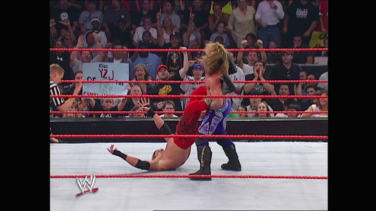 A frame from WWE Raw (August 23, 2004) at 42:20. A WWE wrestler in red attire executes a move on an opponent in purple inside the ring, with a referee present and an enthusiastic crowd visible in the background behind the red ropes.
