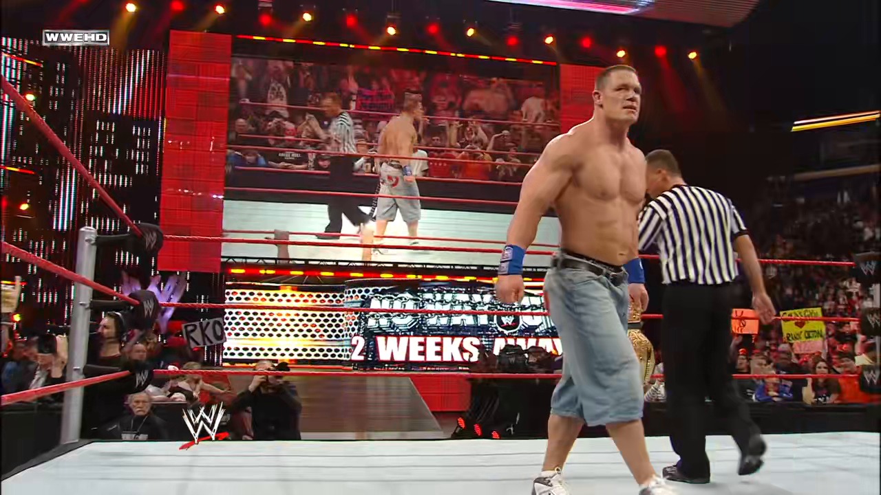 A frame from WWE Raw (February 2, 2009) at 1:29:17. A shirtless WWE wrestler stands in the ring with blue wrist tape, facing the crowd during Raw. A referee in striped shirt stands nearby as the arena glows with red lighting and the WWE logo is visible on the mat.