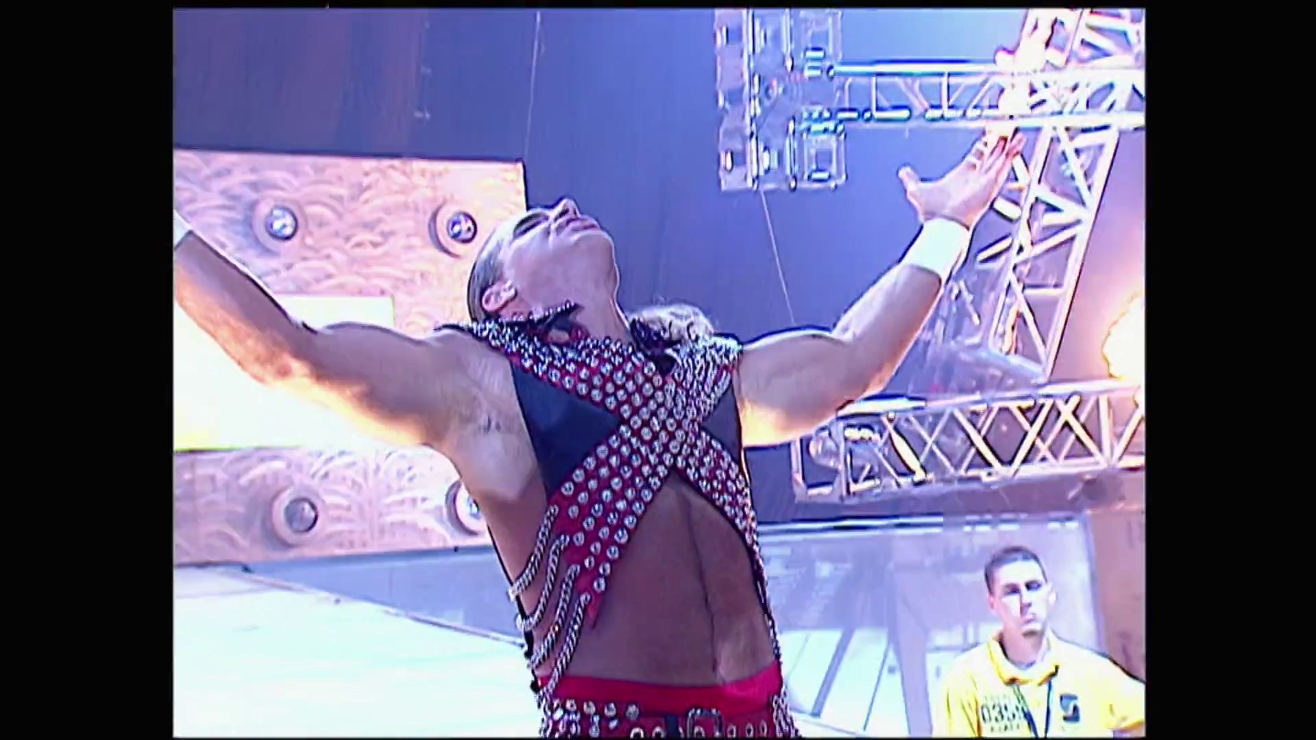 A frame from WWE Raw (January 16, 2006) at 1:18. A wrestler in a burgundy and silver studded outfit stands with arms raised triumphantly in the ring, with an official in a yellow shirt visible nearby and ornate set graphics featuring decorative panels and metal framework in the background.