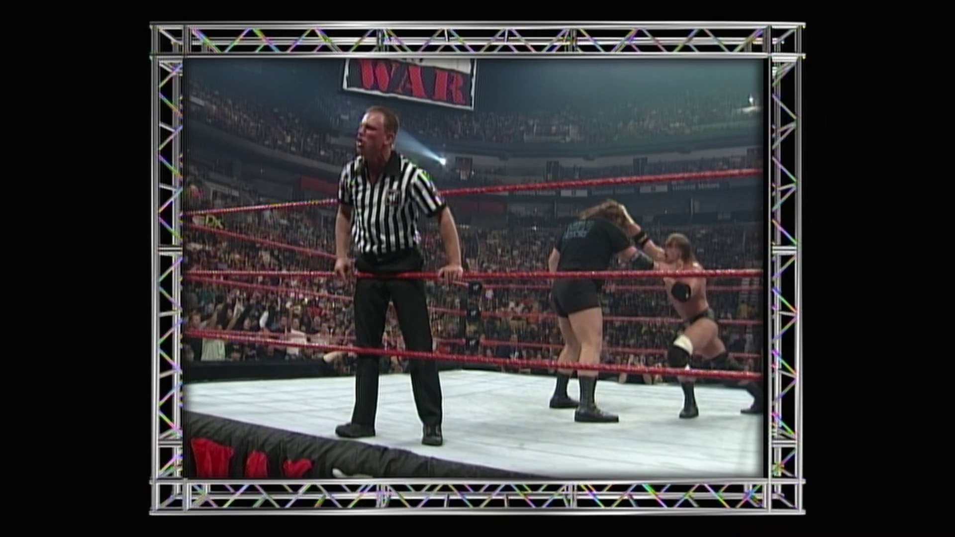 A frame from WWE Raw (January 3, 2000) at 54:32. A referee in black and white striped shirt stands in a WWE wrestling ring with red ropes, overseeing two wrestlers during a match. The packed arena crowd is visible in the background under bright stadium lighting.