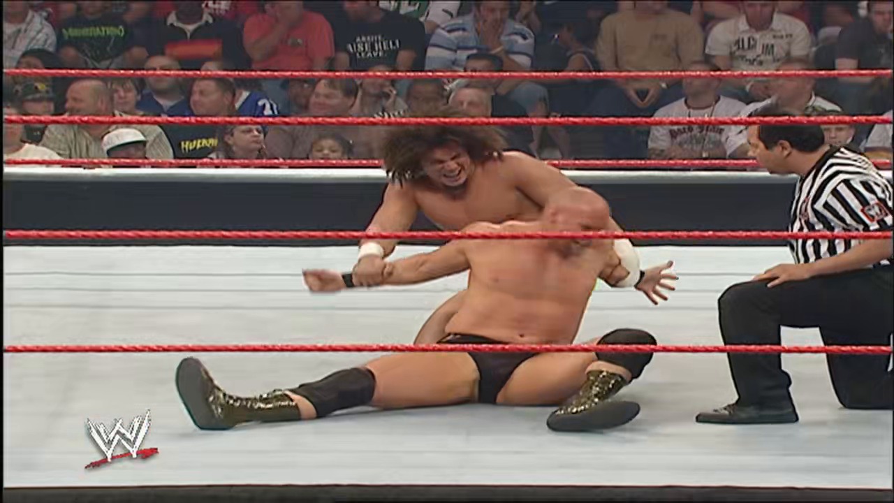 A frame from WWE Raw (May 14, 2007) at 1:02:05. # WWE Raw Match Frame

Two shirtless wrestlers compete in a WWE Raw match on the iconic red and white ring. One wrestler is on the mat while the other stands nearby, with a referee in striped shirt observing as the crowd watches from the stands behind the red ropes.