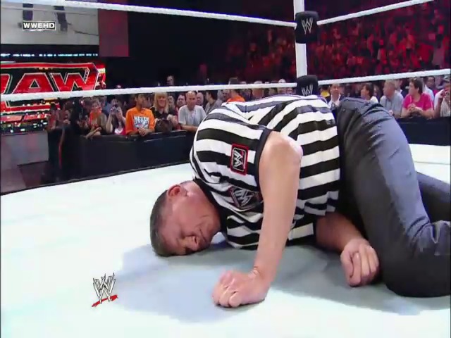 A frame from WWE SmackDown (June 25, 2010) at 37:04. A WWE referee in a black and white striped shirt lies face-down on the wrestling ring during SmackDown, with a live crowd visible in the background and the arena's branding displayed on the overhead graphics.