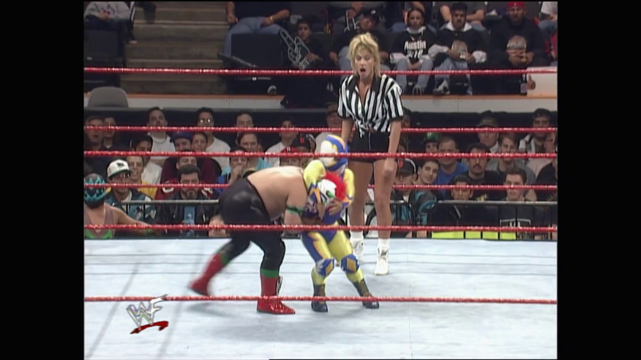 A frame from Royal Rumble (1998) at 23:29. # Visual Description

A WWE wrestling match in progress featuring two wrestlers in the ring with a referee in striped shirt overseeing the action. The red-roped ring is surrounded by an enthusiastic crowd, with the WWF logo visible at ringside.