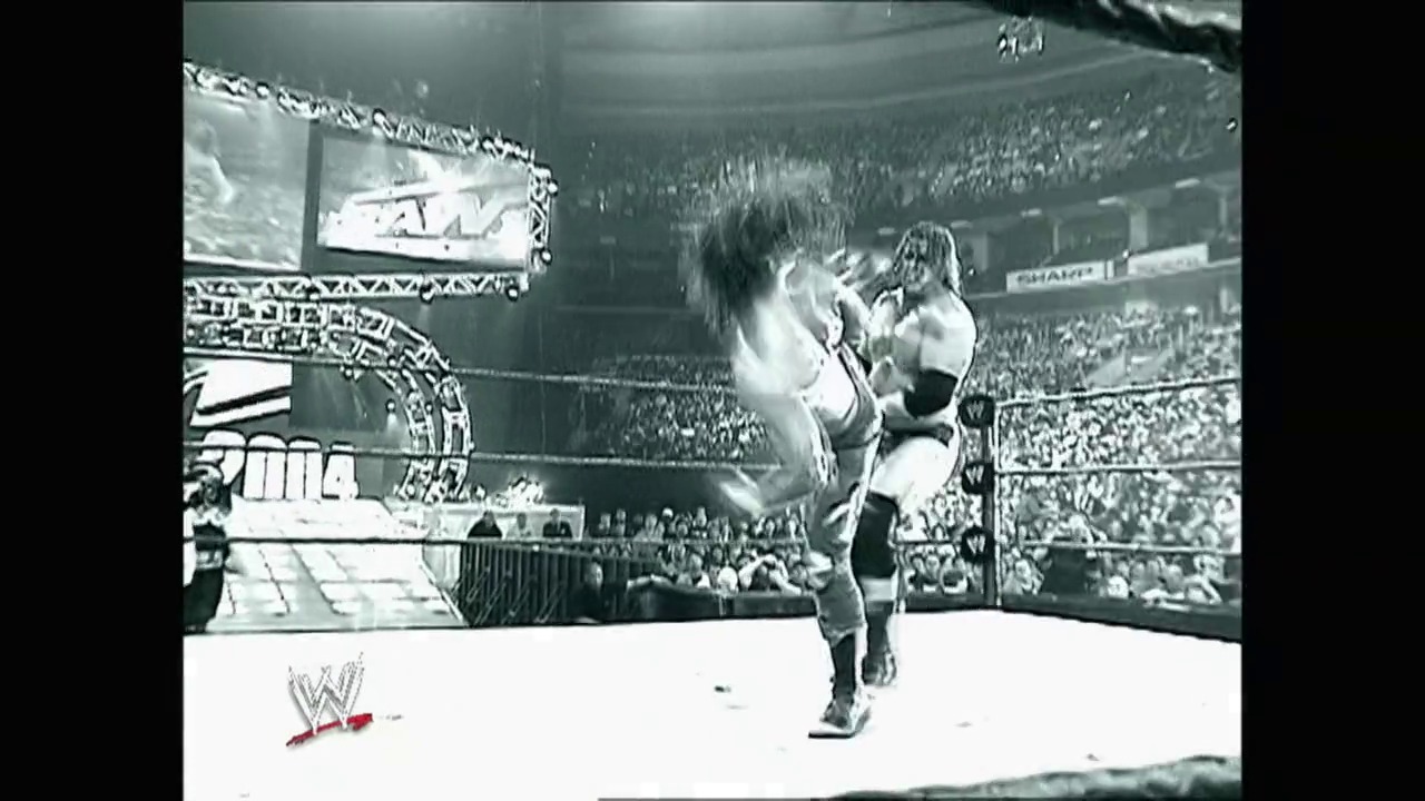 A frame from WrestleMania XX (2004) at 3:51:01. # WrestleMania XX Action Shot

A wrestler executes a high-flying move against an opponent in the ring, with a packed stadium crowd visible in the background. The WWE logo and graphics are displayed on the ring apron and overhead screens during this intense match moment.
