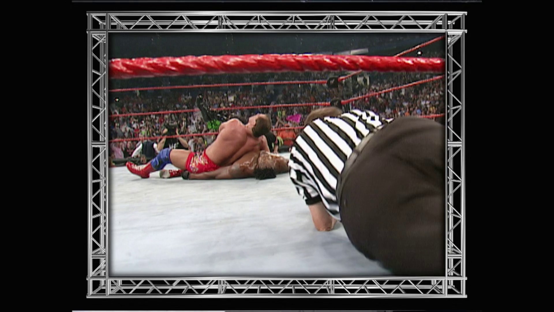 A frame from WWE Raw (July 9, 2001) at 53:10. A wrestler in red attire lies on the mat while a referee in a black and white striped shirt leans over to make a count. The packed arena crowd is visible in the background with red ropes framing the ring.