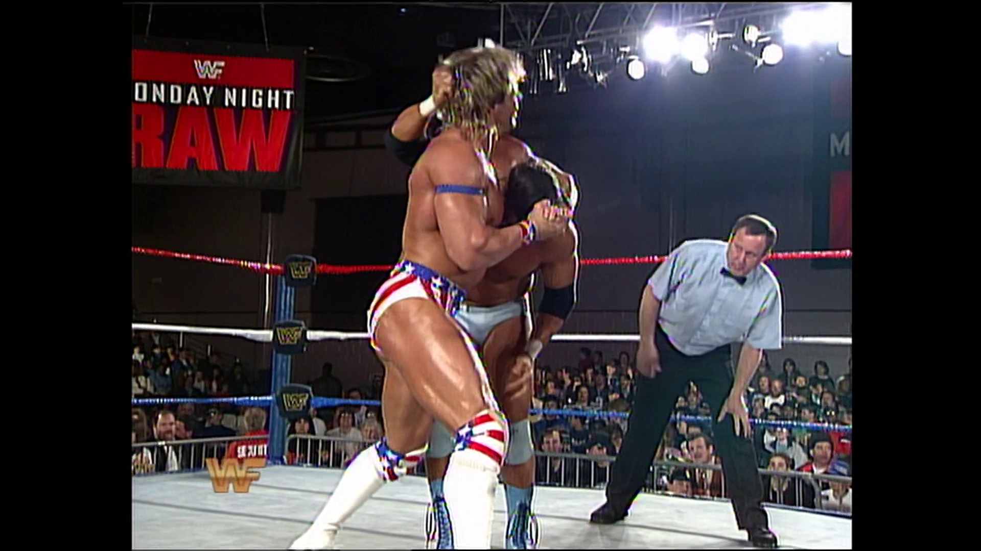 A frame from WWE Raw (March 28, 1994) at 6:46. # WWE Raw Match Scene

Two wrestlers engage in the ring during a Monday Night Raw broadcast, with one performing a move while a referee observes. The crowd watches from the stands as the red and blue roped ring is illuminated under bright arena lights, with the WWF logo visible on the signage.