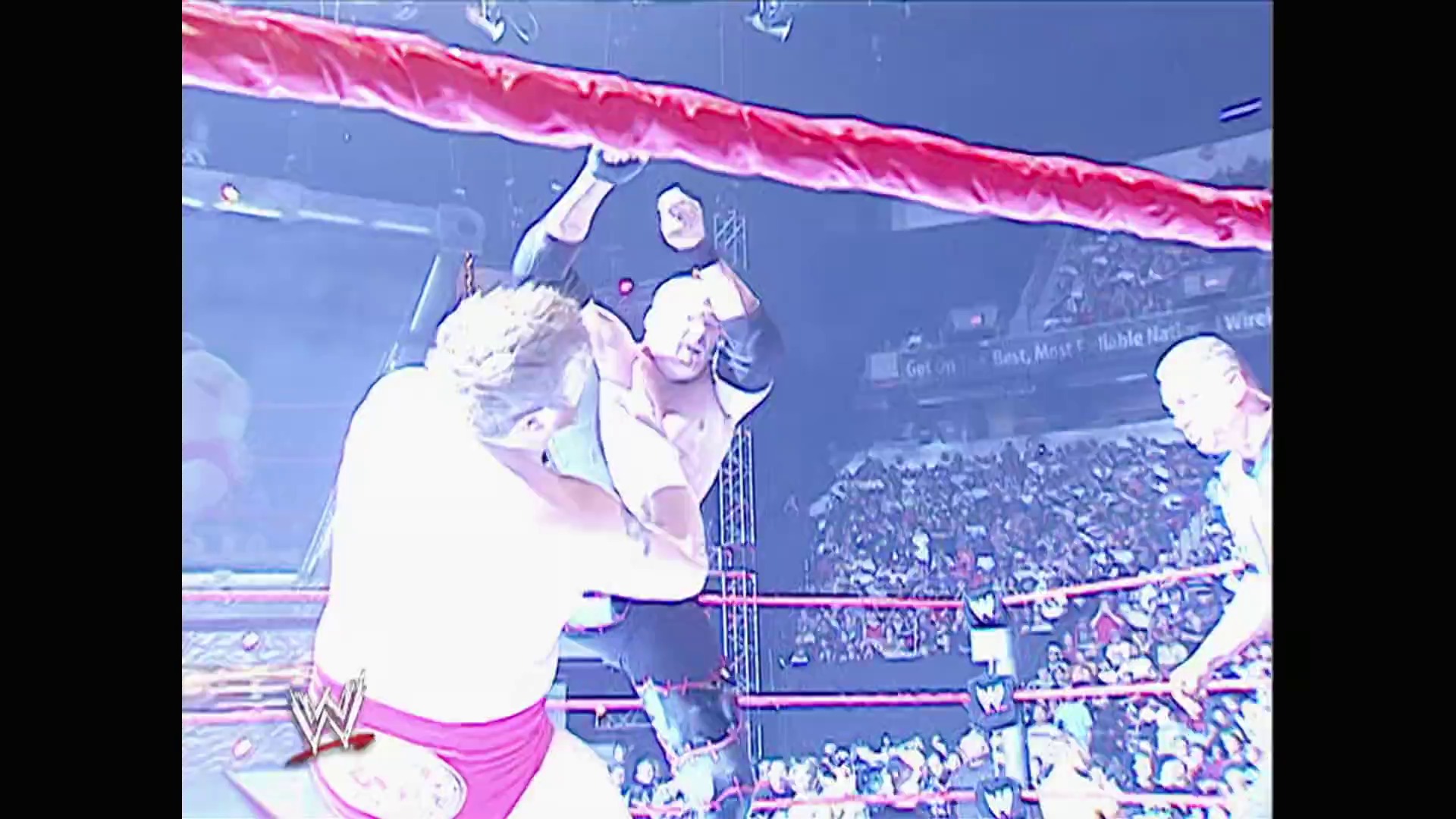 A frame from WWE Raw (May 22, 2006) at 57:16. A shirtless wrestler in pink shorts executes an aerial move in the WWE ring before a packed crowd. The arena features the distinctive red WWE branding and lighting, with spectators visible in the background.