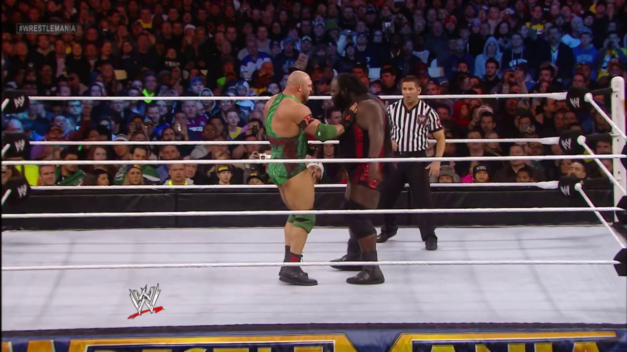 A frame from WrestleMania 29 (2013) at 33:14. Two wrestlers face off in the WWE ring during WrestleMania 29, with one in green attire and the other in dark red, while a referee in striped shirt stands nearby and a large crowd fills the arena behind them.