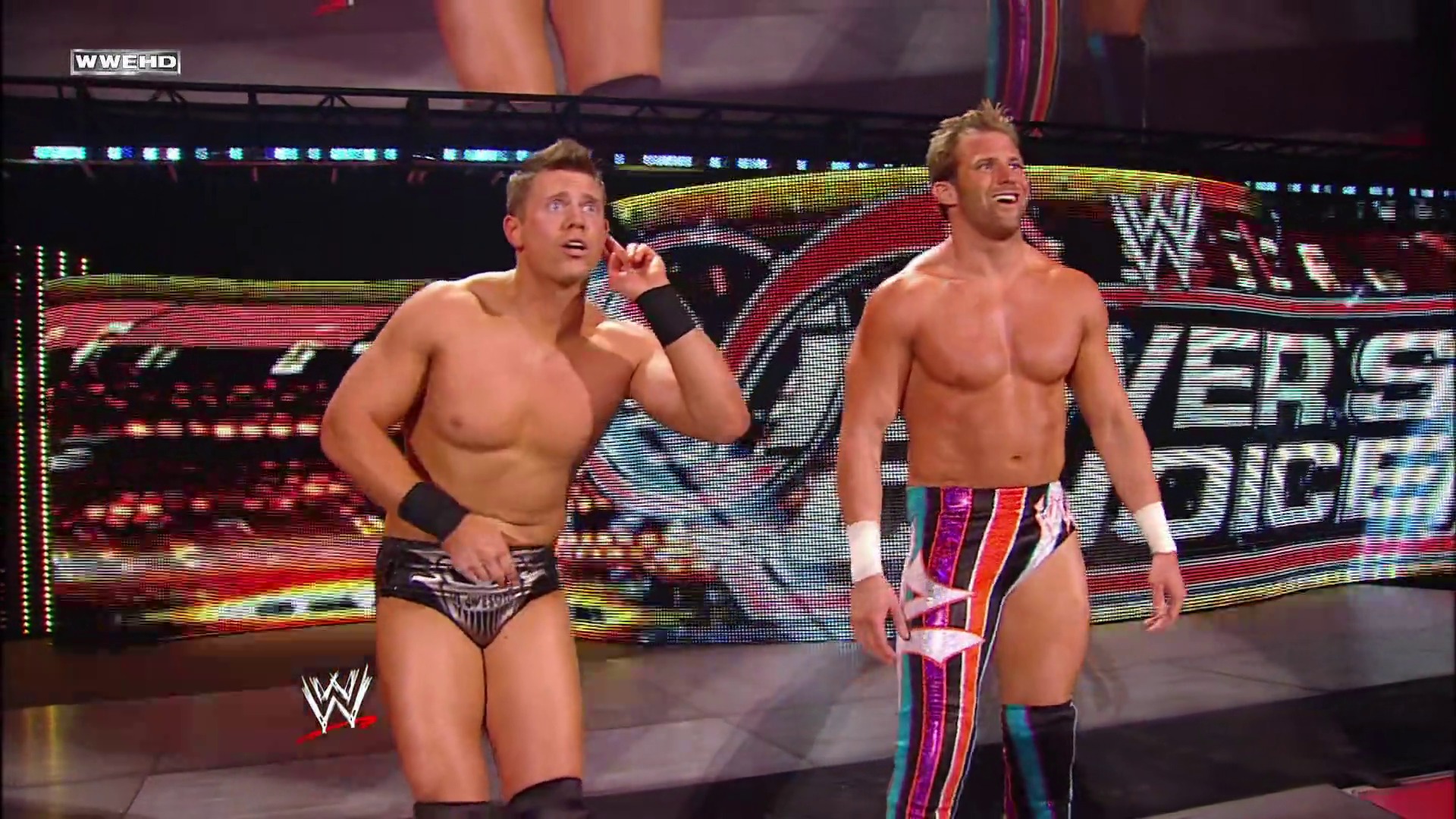 A frame from WWE Raw (June 7, 2010) at 1:16:17. Two shirtless WWE wrestlers stand in the ring during a televised event, with vibrant LED graphics and the WWE logo visible on the backdrop behind them. The scene captures the theatrical presentation typical of professional wrestling entertainment.