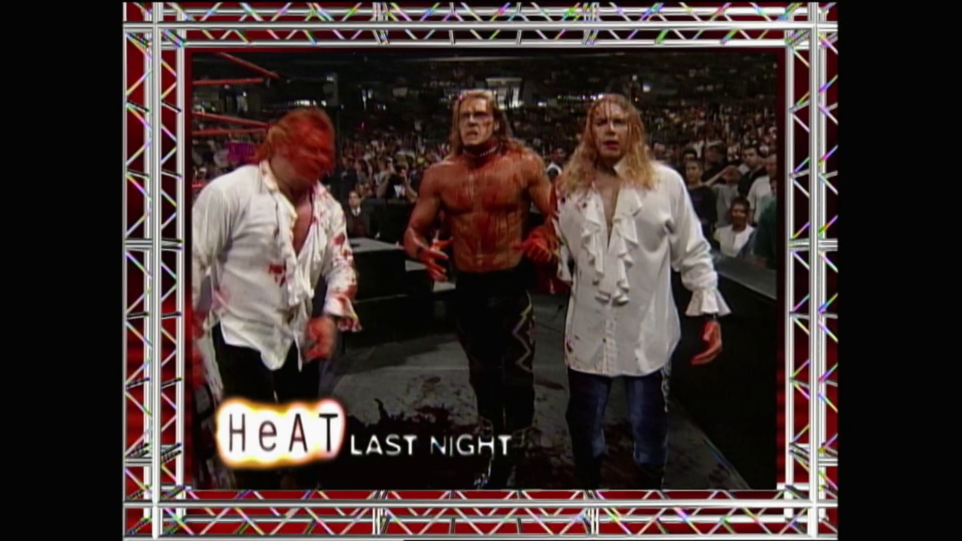A frame from WWE Raw (May 17, 1999) at 54:32. # Visual Description

Three wrestlers stand in the ring during WWE Raw, with two wearing white shirts and one shirtless in the center. The caption reads "HeAT LAST NIGHT" with a large crowd visible in the background and ornate red and silver framing around the broadcast footage.