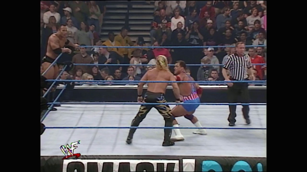 A frame from WWE SmackDown (February 24, 2000) at 1:27:30. A WWE wrestling match is underway in a blue-roped ring with two shirtless wrestlers facing off while a referee watches. The crowd fills the arena in the background, and the WWE SmackDown logo is visible at the bottom of the screen.