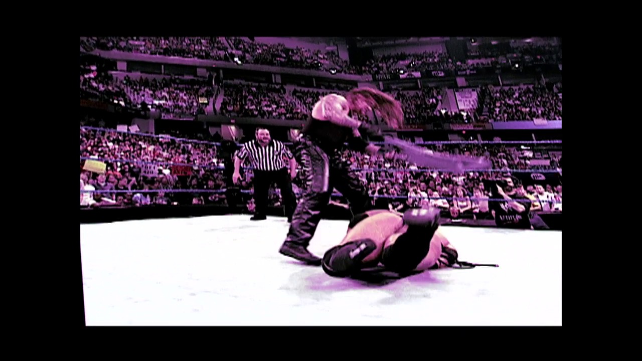 A frame from WWE SmackDown (May 10, 2001) at 0:44. A wrestler lies on the white canvas while a referee in striped shirt stands nearby in a packed arena. The crowd fills the stadium seats in the background under purple-tinted lighting.