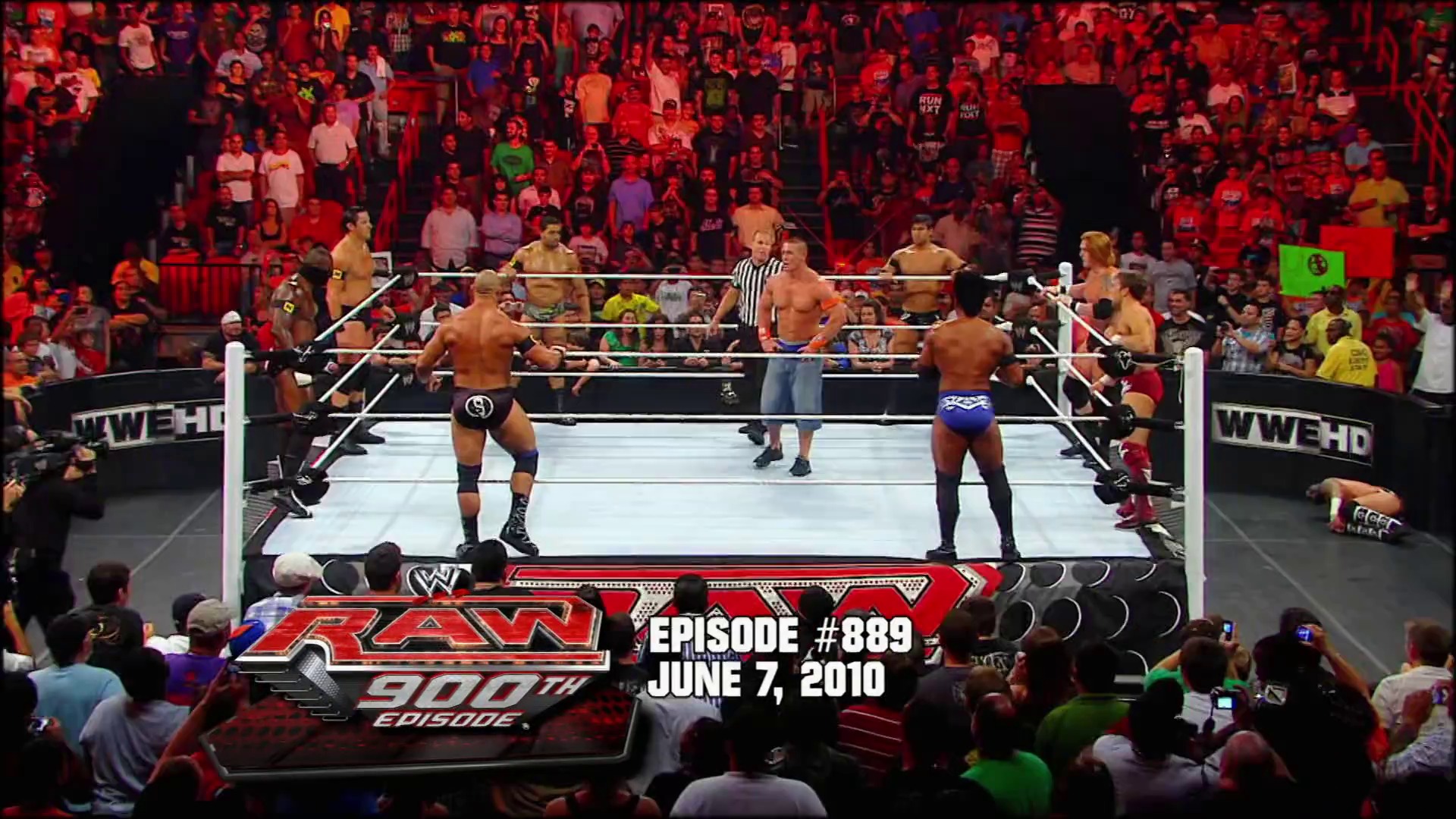 A frame from WWE Raw (August 30, 2010) at 27:29. # WWE Raw Episode #889

A multi-wrestler match unfolds in the ring with shirtless competitors facing off before a packed, enthusiastic crowd bathed in red lighting. The WWE HD graphics and ring setup are clearly visible, with a referee in striped shirt overseeing the action.