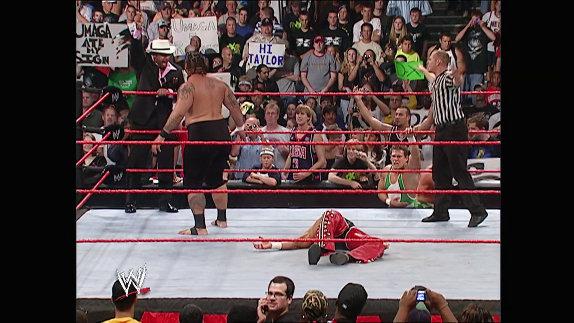 A frame from WWE Raw (July 24, 2006) at 1:05:08. A WWE wrestler in red attire lies on the canvas after being knocked down, while an opponent stands nearby. A referee in a striped shirt oversees the match as the crowd cheers from the stands around the red-roped ring.