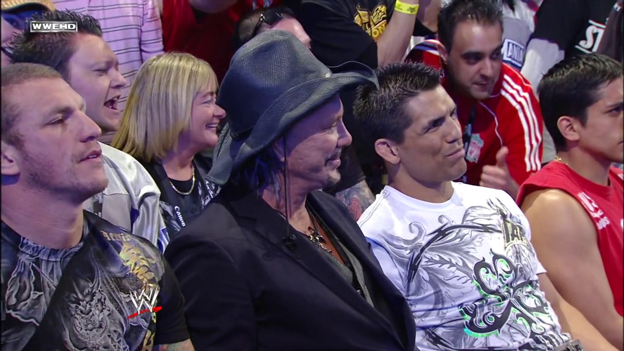 A frame from The 25th Anniversary of WrestleMania (2009) at 1:08:21. A group of WWE wrestlers and personalities are gathered together at ringside, smiling and appearing engaged with the crowd. The scene captures a celebratory moment during WrestleMania 25, with various performers in casual attire mingling among the audience.