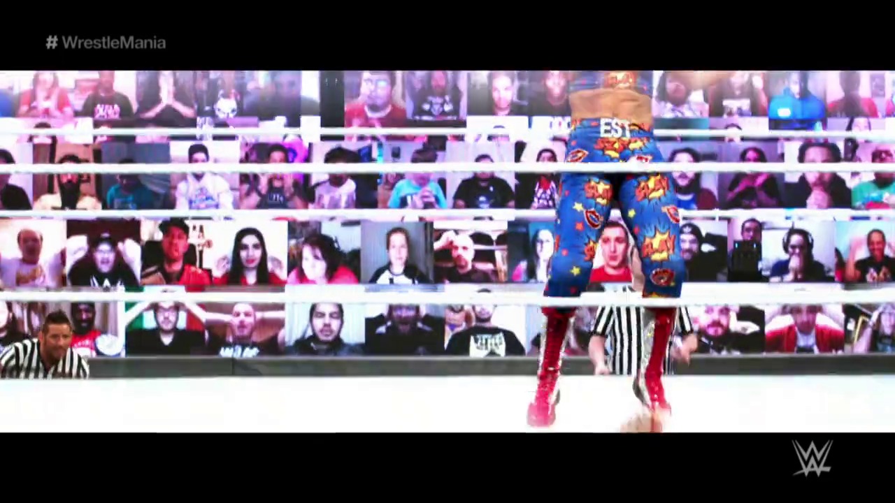 A frame from WrestleMania 37 (2021) at 2:42:04. A WWE wrestler in red and blue attire stands in the wrestling ring during WrestleMania 37, with virtual crowd screens displayed behind the ropes featuring remote fans watching the event.