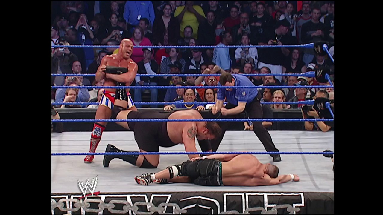 A frame from WWE No Way Out (2004) at 1:45:36. A WWE wrestler in red and white attire stands in the ring while two opponents are down on the mat during an intense match. The crowd fills the arena behind the blue-roped ring, with the WWE logo visible at the bottom of the frame.