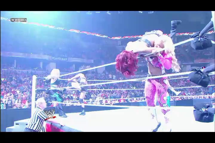 A frame from WWE Raw (August 1, 2011) at 26:08. A WWE wrestler in a vibrant pink and white outfit performs in the ring during Raw, with the referee in striped shirt nearby and a packed crowd visible in the arena background. The WWE branding and arena lighting are visible in the scene.