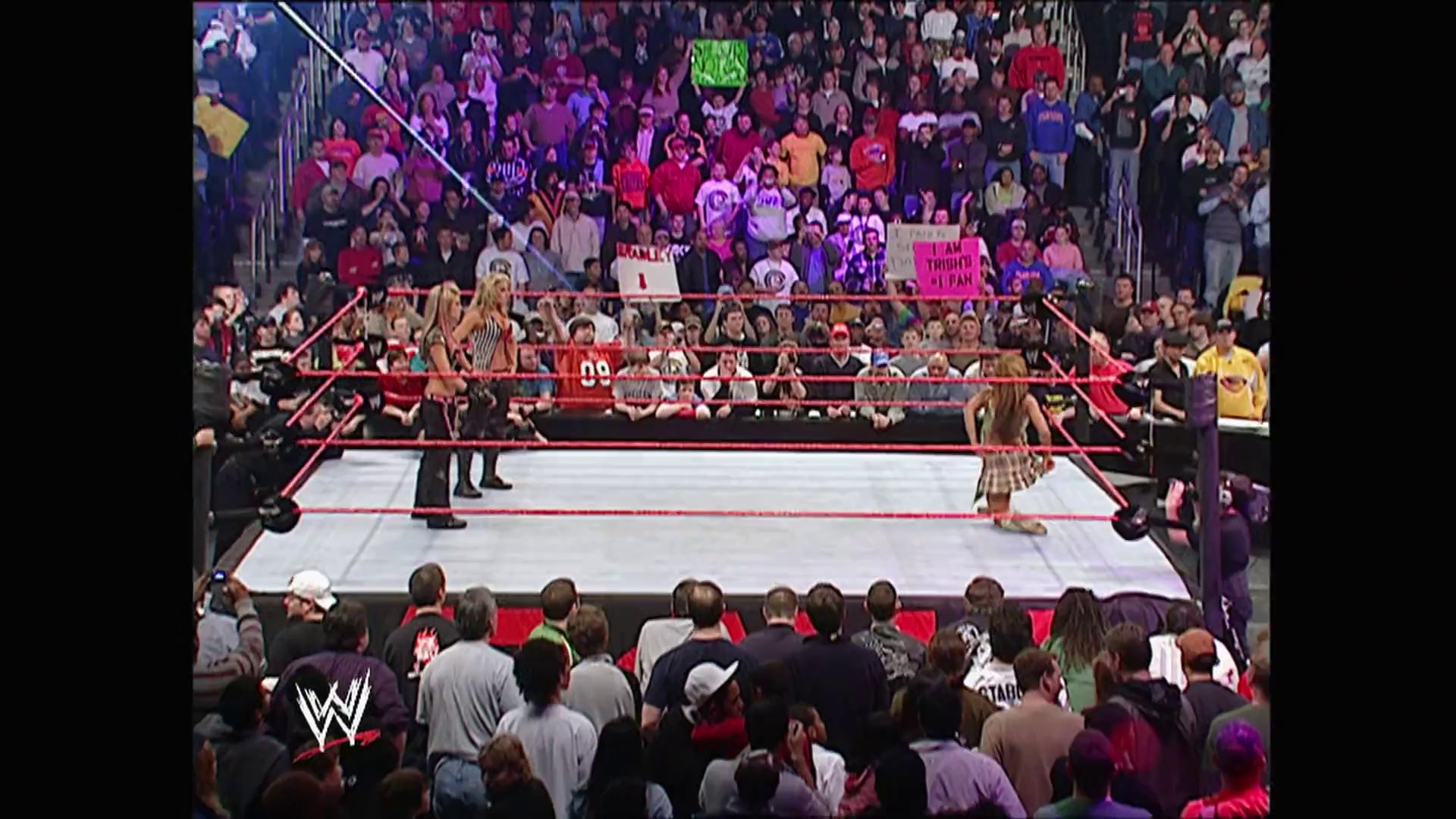 A frame from WWE Raw (February 6, 2006) at 25:05. A WWE Raw wrestling match in progress with two wrestlers in the ring, surrounded by red ropes and a packed crowd. The arena is filled with enthusiastic fans, with the WWE logo visible in the corner and various signs held by spectators in the stands.