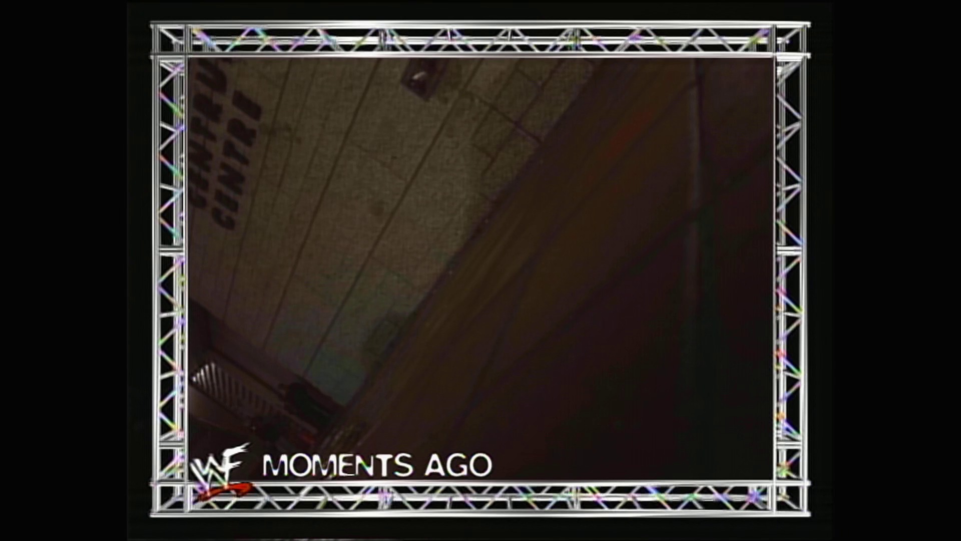 A frame from WWE Raw (January 4, 1999) at 1:18:28. A WWE Raw broadcast frame from January 4, 1999 featuring the WWF logo and "MOMENTS AGO" caption, with an industrial-style metal truss frame border typical of the era's production design.