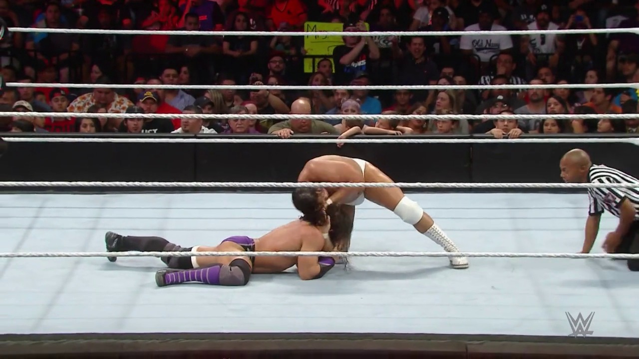 A frame from WWE Raw (June 1, 2015) at 1:55:08. A WWE wrestler lies on the mat in the ring wearing purple and black attire, while a referee in a striped shirt stands nearby. The crowd watches from the stands behind the white ropes of the wrestling ring.