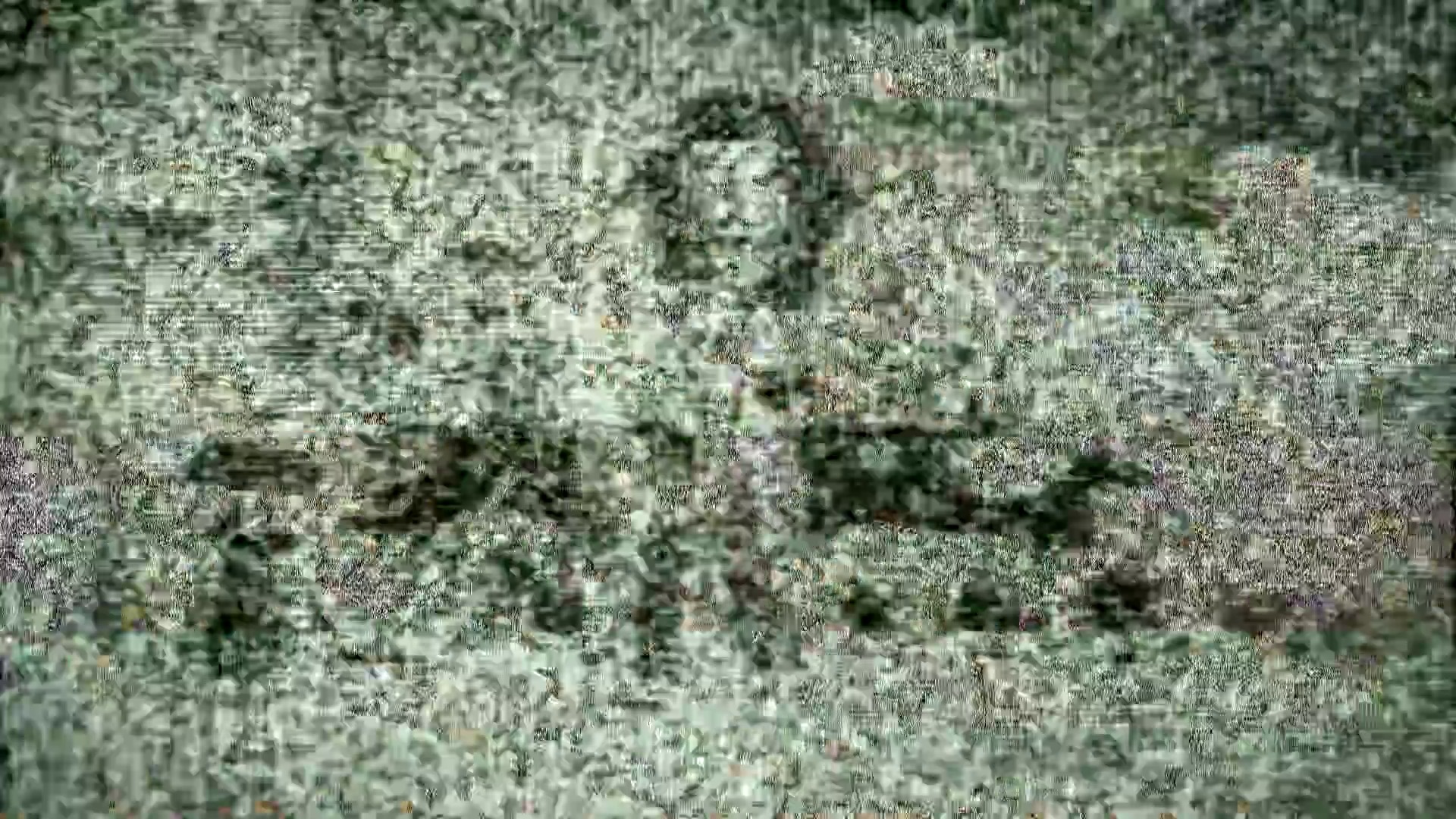 A frame from WWE SmackDown (July 24, 2020) at 24:09. I can see this image is highly pixelated and blurry, making it difficult to discern specific details about the WWE SmackDown event. The image appears to show a wrestling ring environment with green and darker tones, but the resolution is too degraded to clearly identify wrestlers, crowd members, or other specific event elements.