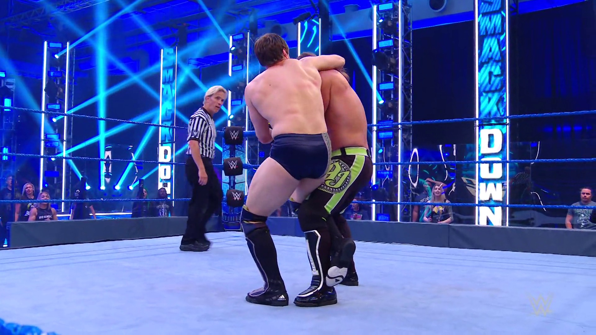 A frame from WWE SmackDown (June 12, 2020) at 31:33. A shirtless wrestler in black and neon green attire performs in a WWE SmackDown ring, with a referee in striped shirt observing nearby. The arena features blue lighting, digital graphics, and audience members visible around the ring perimeter.