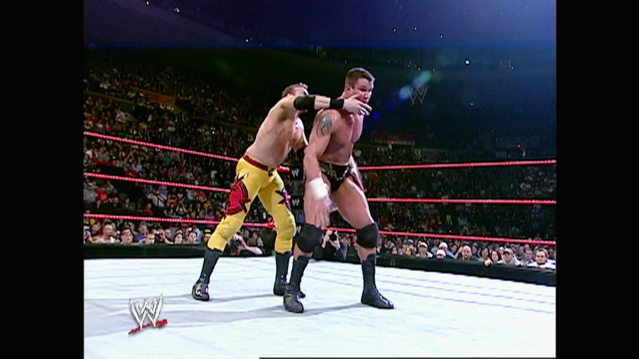 A frame from WWE Raw (February 14, 2005) at 50:35. Two wrestlers grapple in a WWE ring during an intense match, with one opponent applying a headlock while the crowd watches from the stands. The distinctive red ropes frame the action on the mat, with the WWE logo visible on the ring apron.