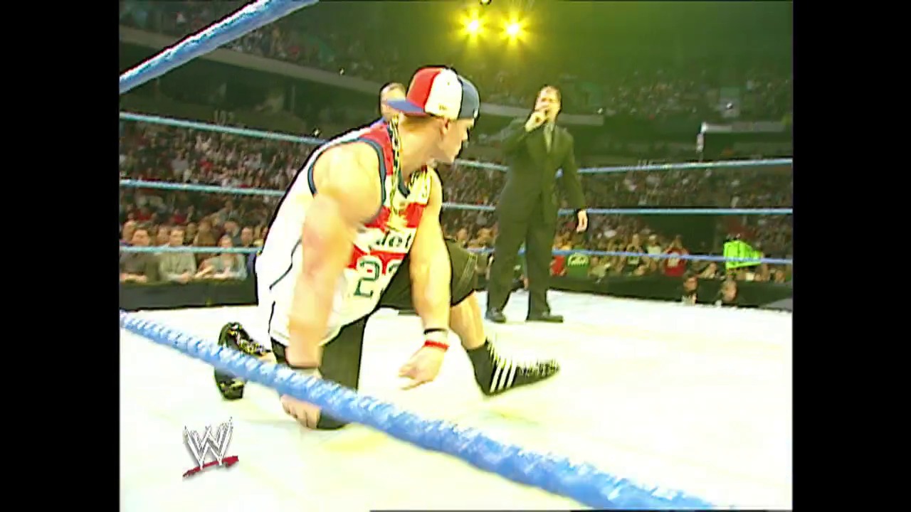 A frame from WWE SmackDown (April 3, 2003) at 37:06. A wrestler in red, white, and blue attire kneels in the WWE ring during a SmackDown event, with a referee in the background and a packed crowd visible in the arena stands under bright overhead lights.