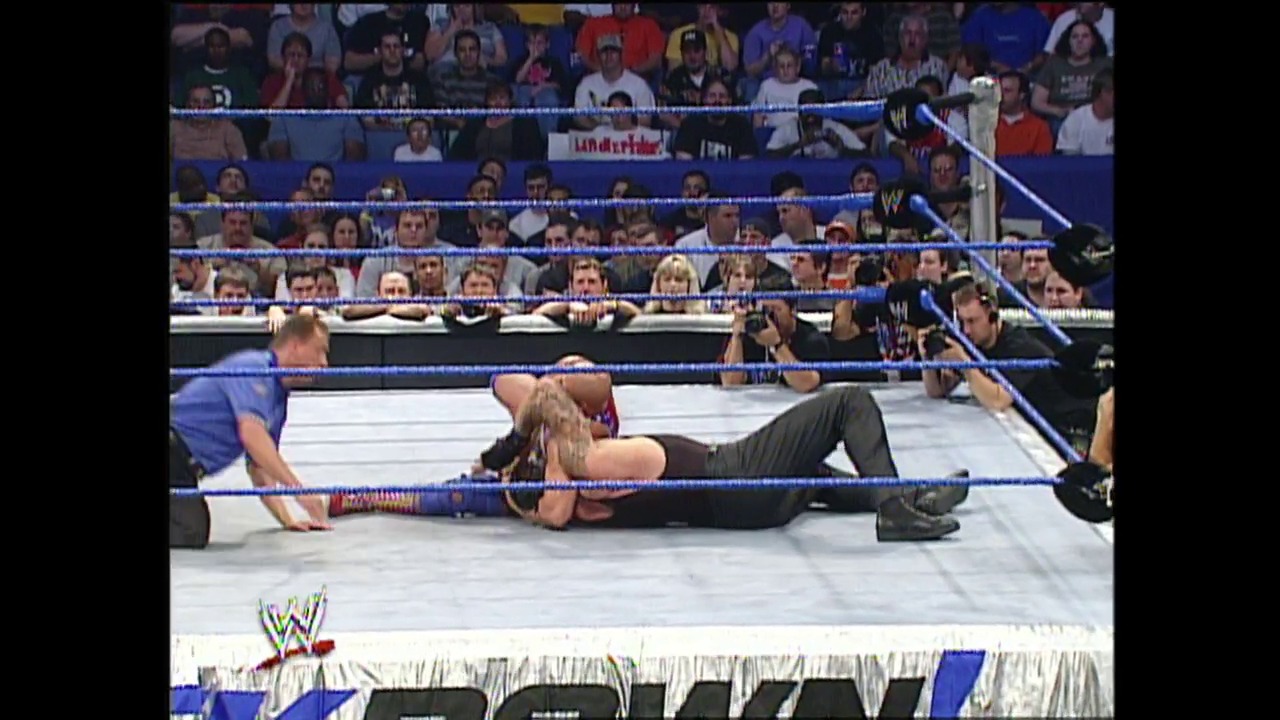A frame from WWE SmackDown (September 4, 2003) at 36:57. A wrestler lies on the mat in a WWE SmackDown ring while another competitor approaches. The blue-roped ring is surrounded by an enthusiastic crowd, with the WWE logo visible at the bottom of the frame.