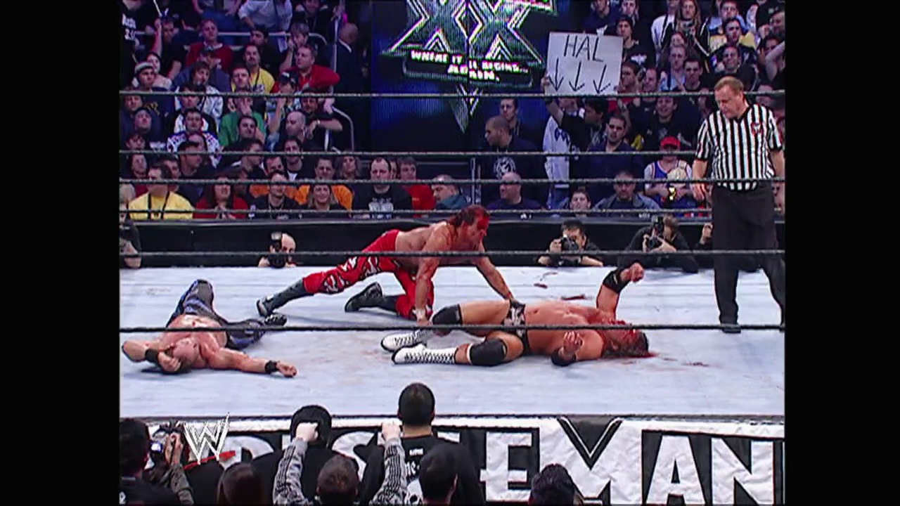 A frame from WWE Raw (December 20, 2004) at 52:33. # WWE Raw Match Scene

Multiple wrestlers lie on the mat during an intense match at WWE Raw, with a referee in striped shirt overseeing the action. The packed arena crowd watches from the bleachers as the event graphics and WWE branding are visible around the ring.
