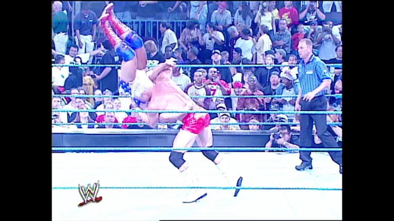 A frame from WWE Raw (September 19, 2002) at 1:12:52. A WWE wrestler in pink and blue attire performs an acrobatic move in the ring during a live event, with a full crowd visible in the bleachers behind the ropes. A referee in a striped shirt oversees the match as the WWE logo appears in the lower left corner.