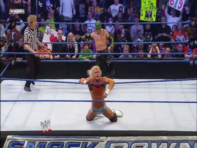 A frame from WWE SmackDown (February 5, 2010) at 1:11:48. A blonde wrestler in red and black attire kneels in the WWE SmackDown ring, celebrating with raised arms while a referee stands nearby and the crowd cheers from the surrounding bleachers.