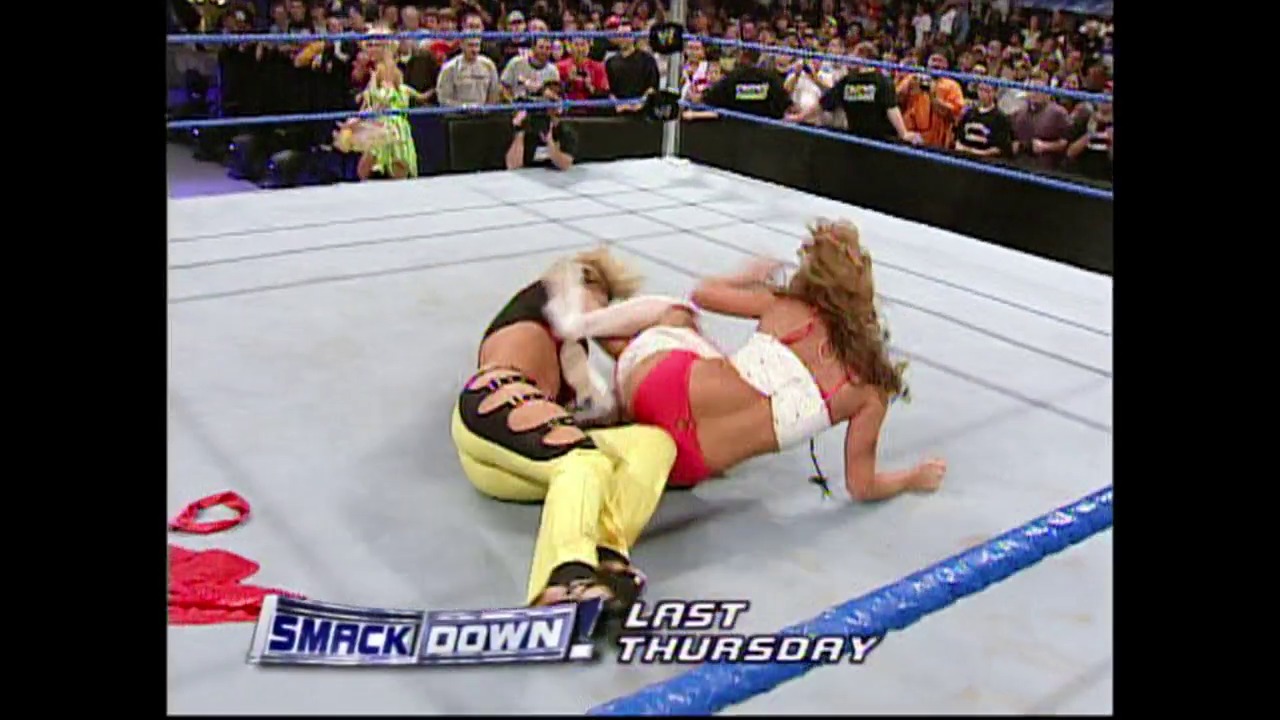 A frame from WWE SmackDown (November 4, 2004) at 1:02:24. # WWE SmackDown Ring Action

Two wrestlers grapple on the mat during an intense match, with one performer in yellow pants applying pressure while the crowd watches intently from the surrounding seats. The blue-roped ring and "SmackDown Last Thursday" graphic are visible at the bottom of the frame.