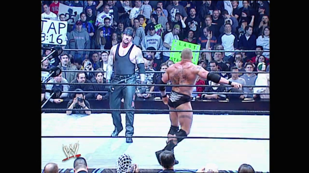 A frame from Royal Rumble (2003) at 2:37:04. Two wrestlers face off in a WWE ring during the 2003 Royal Rumble event, with one shirtless competitor squaring up against another in wrestling attire. A packed crowd fills the arena stands behind the ropes, while the WWE logo and match timer display at the bottom of the screen.