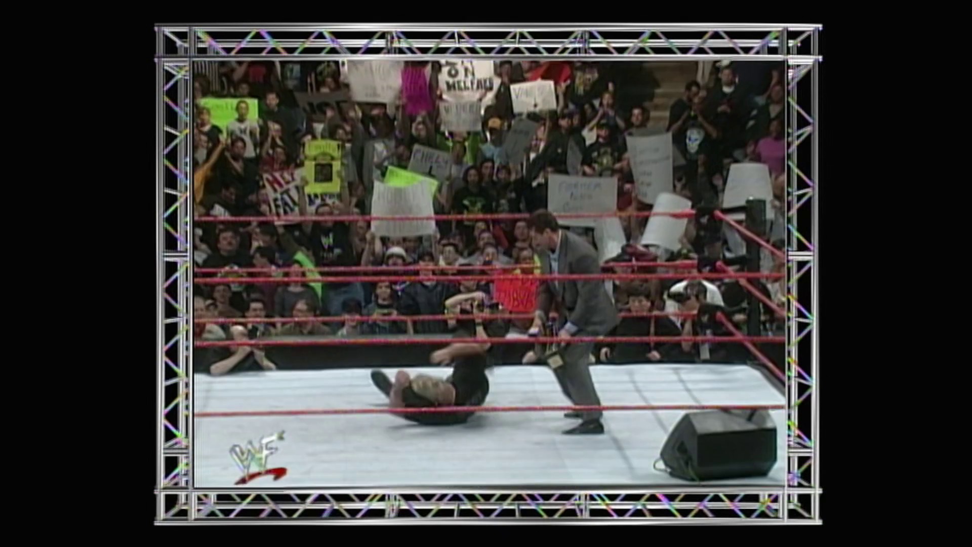 A frame from WWE Raw (March 29, 1999) at 15:10. A WWE wrestler lies on the mat in the ring while an opponent stands nearby during a match. The crowd fills the stands above, some holding signs, with the red ropes and white mat visible in this classic late-90s wrestling broadcast.