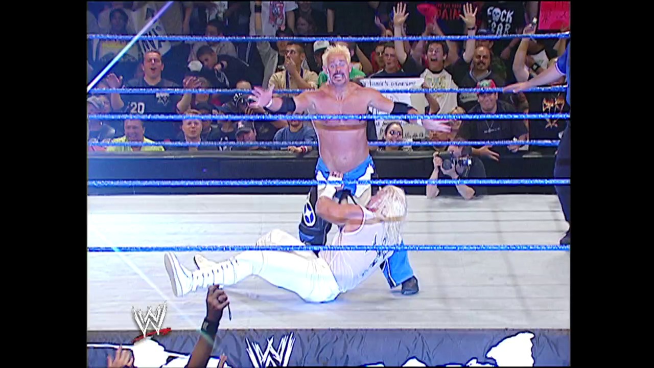 A frame from WWE Judgment Day (2004) at 45:28. # WWE Judgment Day (2004) Frame

A blonde wrestler in blue and white attire stands victoriously in the ring while an opponent lies on the mat below. The crowd in the background cheers enthusiastically behind the blue-roped wrestling ring, with WWE branding visible at the bottom of the frame.